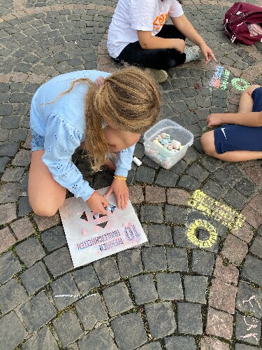 Ein Kind sitzt auf auf dem Boden des Bonner Münsterplatzes. MIthilfe einer Schablone und Kreide malt es das SDG 10 auf den Boden.